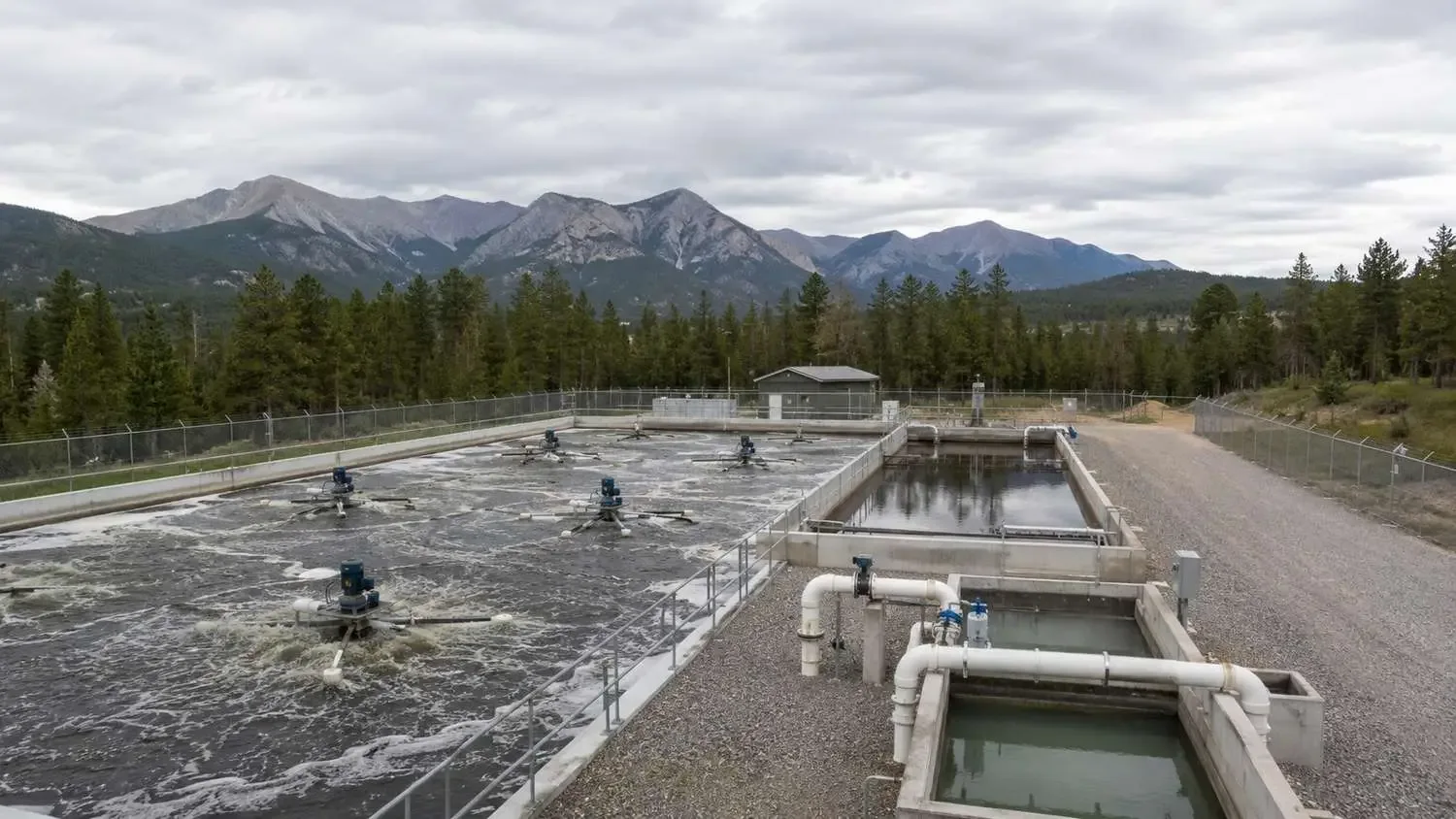 Ground-level shot of a Colorado package wastewater treatment plant with an extended aeration basin, surface aerators and a secondary clarifier in a mountain setting.
