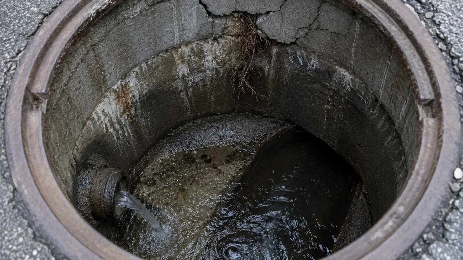 Cracked concrete sewer manhole in a small Texas community showing visible groundwater infiltration entering the collection system through deteriorated joint connections